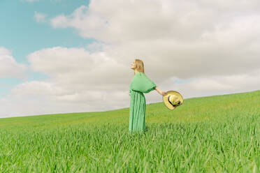 Blonde junge Frau in grünem Kleid steht auf einem Feld - ERRF03297