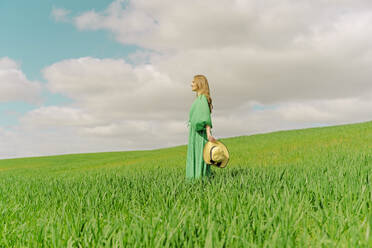 Blonde junge Frau in grünem Kleid steht auf einem Feld - ERRF03298