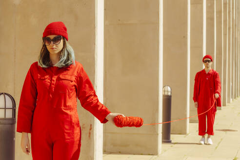 Young couple wearing red overalls and hats standing in a row connected with red string - ERRF03320