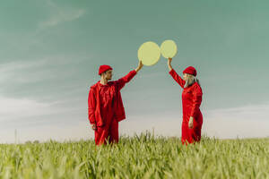 Junges Paar in roten Overalls steht auf einem Feld und hält zwei grüne Kreise - ERRF03355