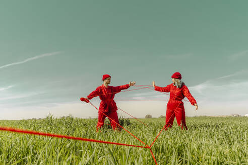 Young couple wearing red overalls and hats performing on a field with red string - ERRF03368