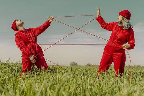 Young couple wearing red overalls and hats performing on a field with red string - ERRF03370