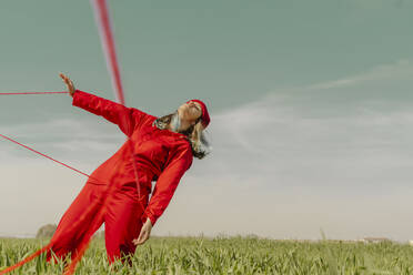Junge Frau in rotem Overall und Hut auf einem Feld mit roter Schnur - ERRF03372