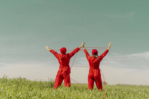 Rückenansicht eines jungen Paares in roten Overalls und Hüten, das auf einem Feld mit roter Schnur auftritt, lizenzfreies Stockfoto