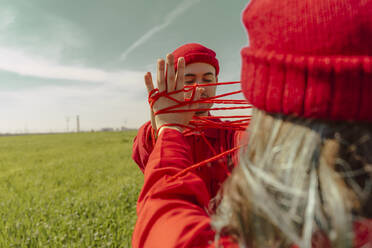 Young couple wearing red overalls and hats performing on a field with red string - ERRF03379