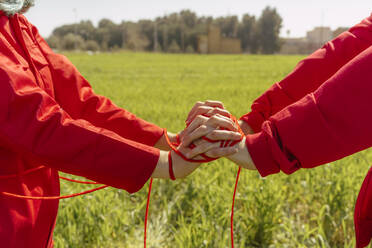 Crop view of young couple dressed in red performing on a field with red string - ERRF03381