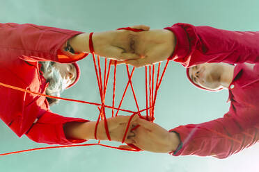 Crop view of young couple dressed in red performing with red string against sky - ERRF03383