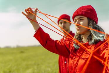 Portrait of young woman dressed in red performing with red string outdoors - ERRF03385