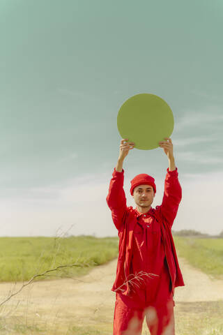 Porträt eines rot gekleideten jungen Mannes, der einen grünen Kreis hält, lizenzfreies Stockfoto