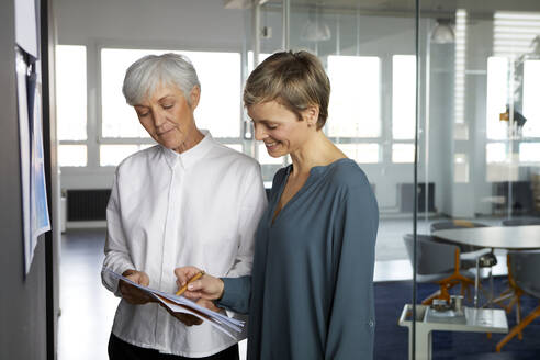 Zwei Geschäftsfrauen arbeiten im Büro gemeinsam an einem Papier - RBF07358