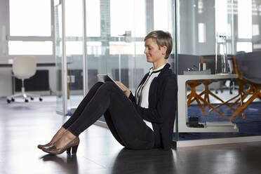 Geschäftsfrau sitzt auf dem Boden im Büro und benutzt ein Tablet - RBF07368