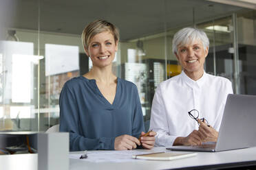 Portrait of two confident businesswomen with laptop in office - RBF07418