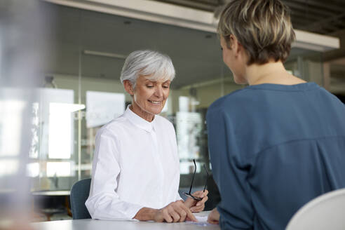 Two businesswomen talking at desk in office - RBF07420