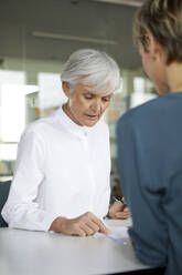 Zwei Geschäftsfrauen im Gespräch am Schreibtisch im Büro - RBF07421