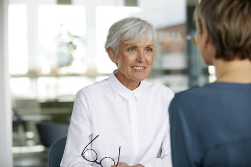 Portrait of senior businesswoman talking to colleague in office - RBF07422