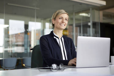 Smiling businesswoman using laptop in office - RBF07434