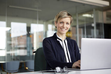 Portrait of smiling businesswoman using laptop in office - RBF07435