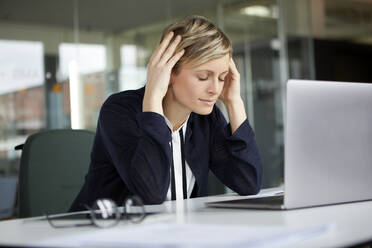 Businesswoman in office with head in hands and closed eyes - RBF07437