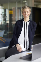 Portrait of smiling businesswoman with laptop in office - RBF07438