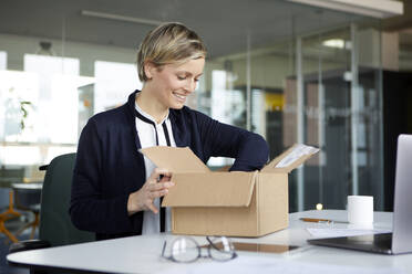 Smiling businesswoman unpacking parcel on desk in office - RBF07441