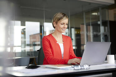 Lächelnde Geschäftsfrau mit Laptop im Büro - RBF07442