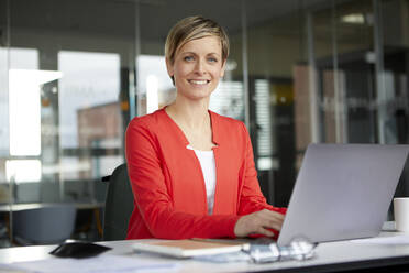 Portrait of smiling businesswoman using laptop in office - RBF07443