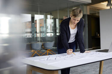 Frau arbeitet an einem Bauplan im Büro - RBF07444