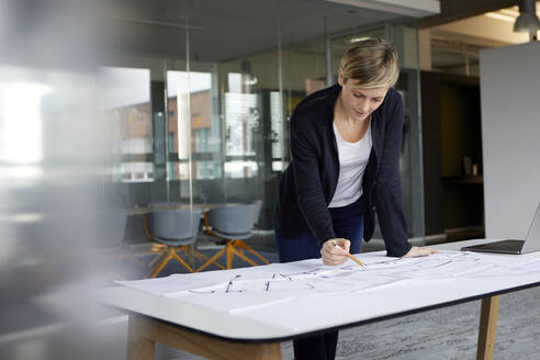 Woman working on construction plan in office - RBF07444