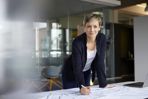 Porträt einer lächelnden Frau, die in einem Büro an einem Bauplan arbeitet - RBF07445