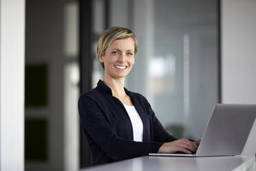 Portrait of smiling businesswoman using laptop in office - RBF07453