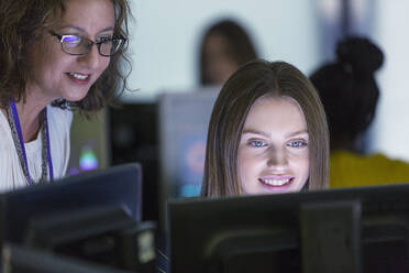 Female junior high teacher helping student at computer in computer lab - CAIF25724
