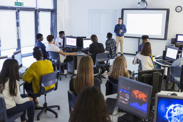 Schüler der Mittelstufe an Computern, die den Lehrer auf der Projektionsfläche im Klassenzimmer beobachten - CAIF25748