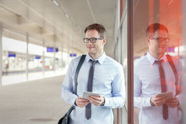 Businessman with digital tablet waiting near train station platform - CAIF25770