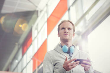 Nachdenklicher junger Mann mit Kopfhörern und mp3-Player - CAIF25772