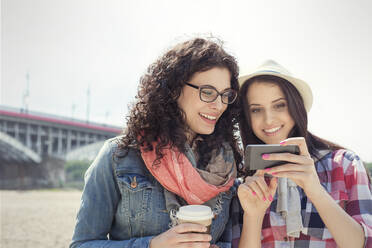 Young women friends using smart phone and drinking coffee outdoors - CAIF25773