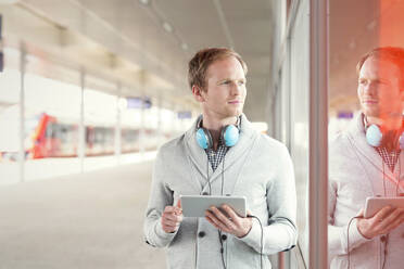 Junger Mann mit digitalem Tablet und Kopfhörern wartet in der Nähe des Bahnsteigs - CAIF25782