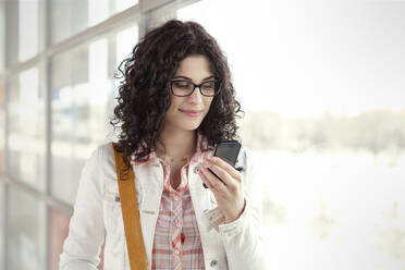 Junge Frau benutzt Smartphone am Fenster - CAIF25786