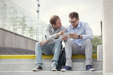 Geschäftsleute im Gespräch, die ein digitales Tablet auf einer Treppe benutzen - CAIF25788
