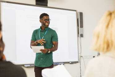 Männlicher Community-College-Lehrer, der eine Unterrichtsstunde an der Projektionsfläche im Klassenzimmer leitet - CAIF25793