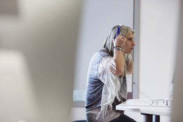 Ältere Studentin passt Kopfhörer am Computer im Klassenzimmer an - CAIF25799