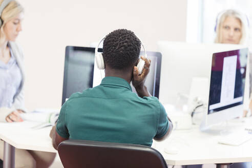 Männlicher Student einer Volkshochschule mit Kopfhörern am Computer im Computerraum - CAIF25897