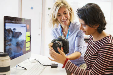 Female photography instructor helping student with digital camera at computer in classroom - CAIF25903