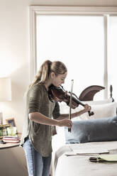 Ein dreizehnjähriges Teenager-Mädchen spielt im Schlafzimmer Geige - MINF14510