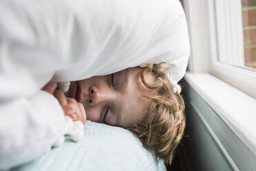 Ein sechsjähriger Junge im Bett mit einer Decke über dem Kopf - MINF14513