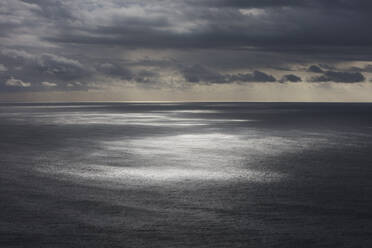 Gewitterwolken, die sich über dem weiten Meer auflösen, gedämpftes Sonnenlicht auf dem Wasser - MINF14543