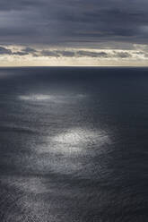 Gewitterwolken, die sich über dem weiten Meer auflösen, gedämpftes Sonnenlicht auf dem Wasser - MINF14544