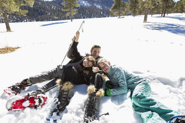 Eine Frau und ihre beiden Kinder, ein Mädchen im Teenageralter und ein kleiner Junge, liegen in Schneeschuhen und Skiausrüstung im Schnee. - MINF14554