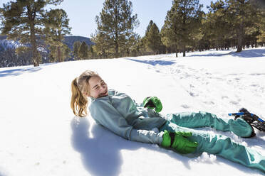 A teenage girl wearing snow shoes lying in the snow laughing - MINF14555
