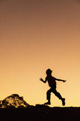 Silhouette carefree boy running against golden sunset sky - FSIF04635