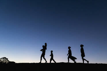 Silhouette Familie zu Fuß gegen blauen Himmel in der Abenddämmerung - FSIF04636